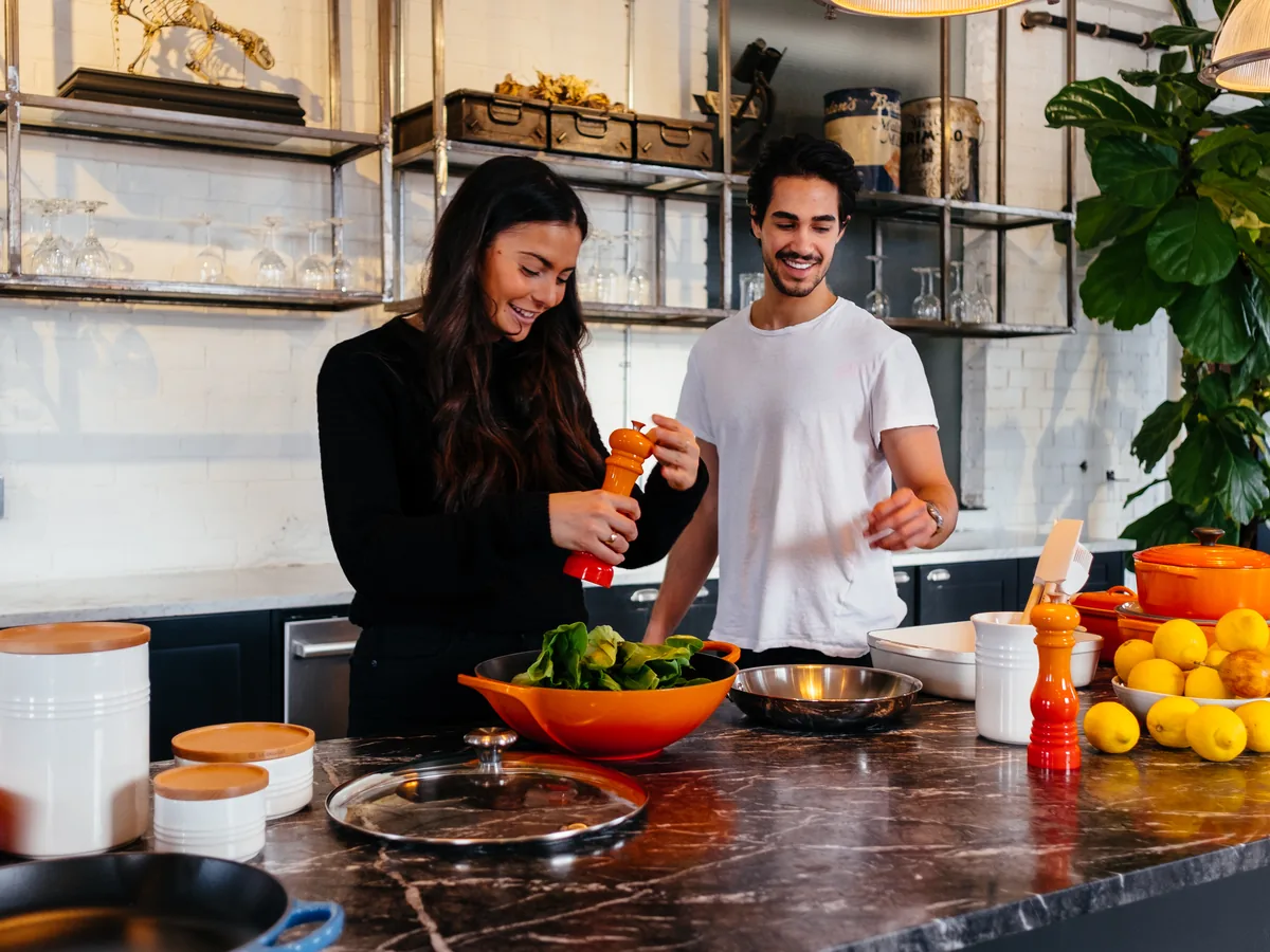 A couple laughing as they cook together in a bright kitchen